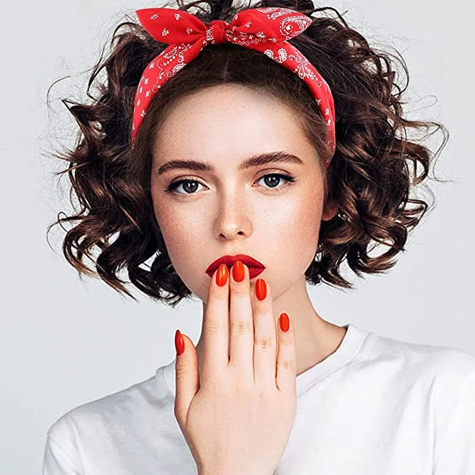 A woman wearing a red paisley bandana headband, covering her mouth with her fingers.