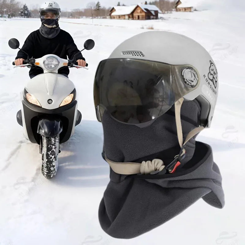 A person wearing a black balaclava and helmet is riding a motorcycle in the snow.