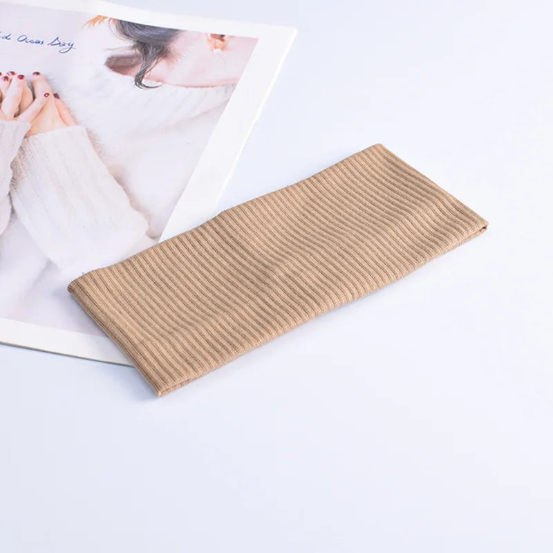 A beige ribbed knitted headband lying next to a magazine featuring a woman's hand and arm.