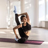 A woman performing a yoga pose on a purple mat wearing black athletic wear and blue grip socks.