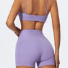 A woman wearing purple high-waist yoga shorts and a matching crop top, shown from the back.