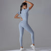 A woman wearing a light blue Naked Zipper Yoga Jumpsuit posing against a gray background.
