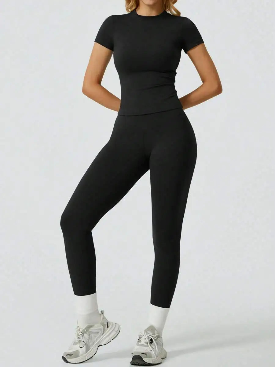 Eine Frau trägt ein schwarzes zwei-teiliges Yoga-Set mit hohen Leggings und einem kurzärmeligen Oberteil.