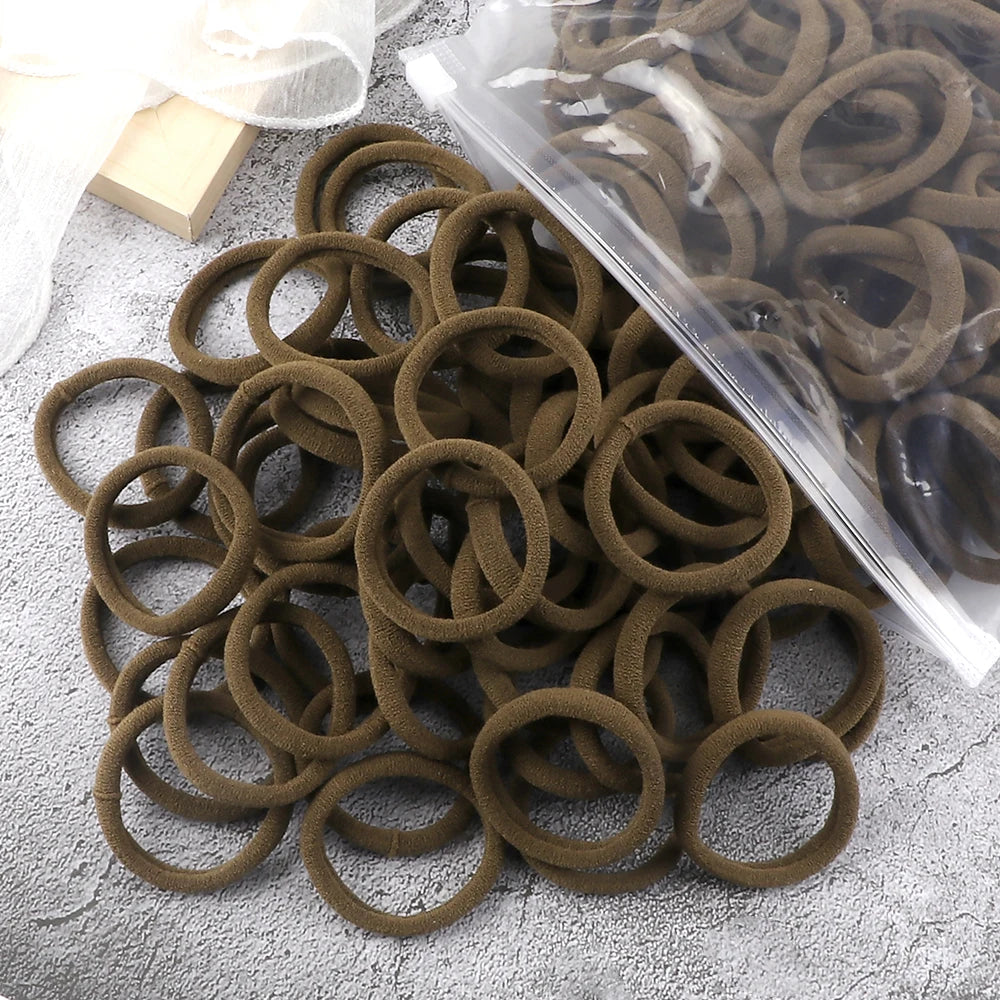 A pile of 50 pieces of mixed color elastic hair bands in a clear plastic bag on a gray surface.