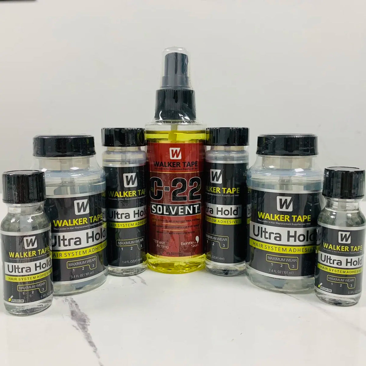 A collection of Walker Tape Ultra Hold lace wig glue bottles in various sizes and colors.