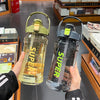 A hand holds a clear insulated sports water bottle with a green cap and a straw, set against a background of books.
