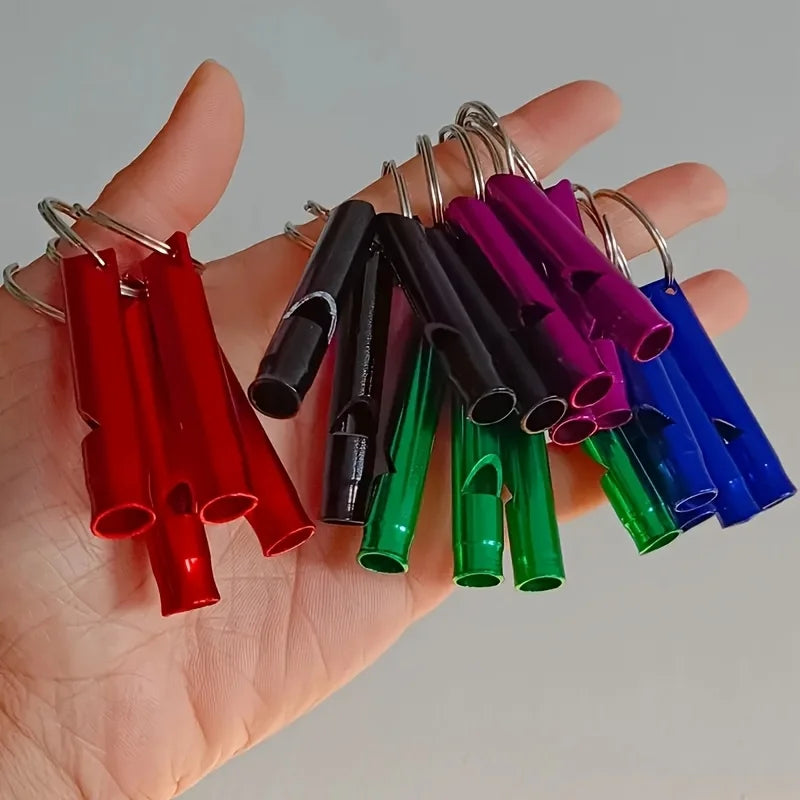 A hand holds a collection of colorful aluminum survival whistles attached to metal clasps.