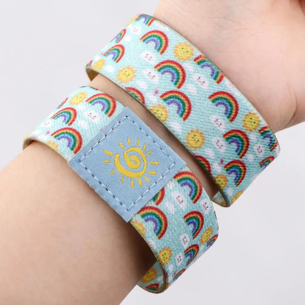 A colorful LGBT stretch wristband bracelet featuring a pattern of rainbows and suns on a light blue background.