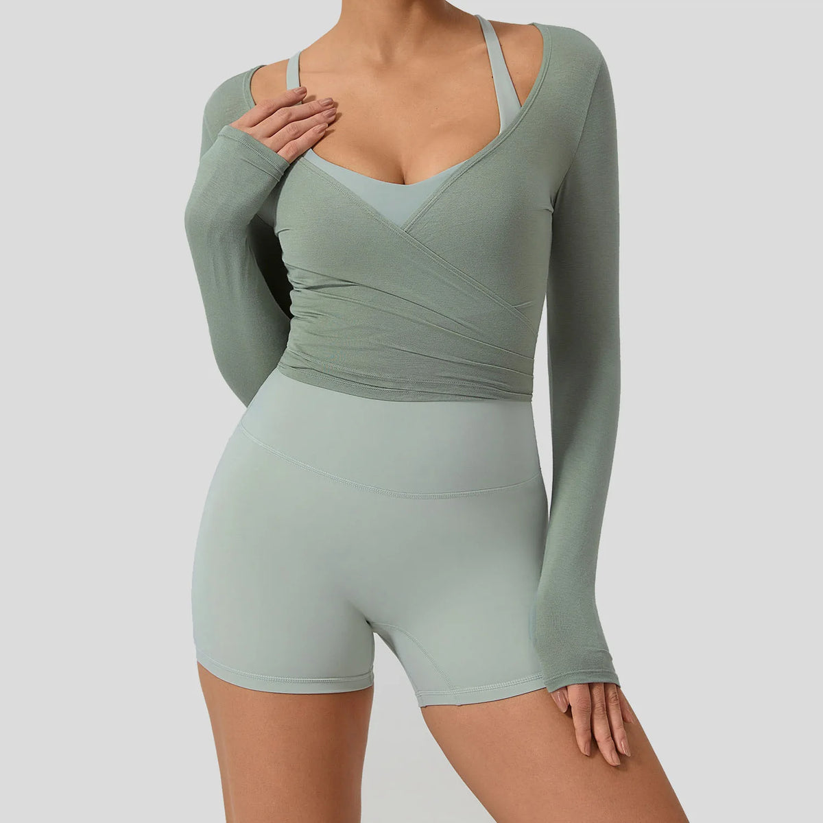 A woman wearing a sage green long sleeve top and matching high-waisted leggings for yoga or sport.