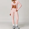 A woman models a pink 3-piece yoga sports set consisting of a long-sleeved cropped jacket, sports bra, and leggings.