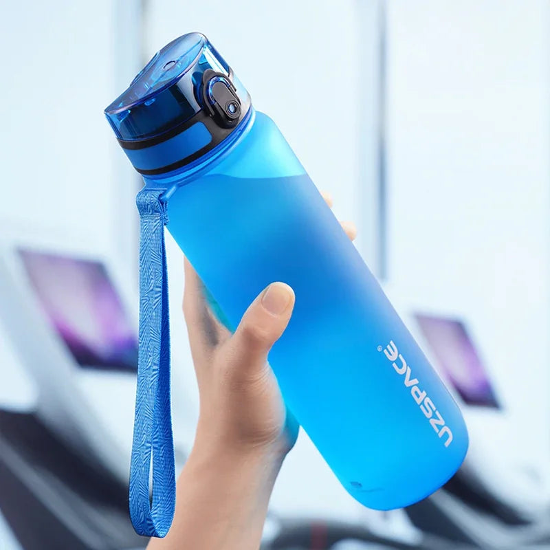 Eine Hand hält eine leuchtend blaue wiederverwendbare Sportflasche mit einem Trageriemen vor einem hellen Hintergrund.