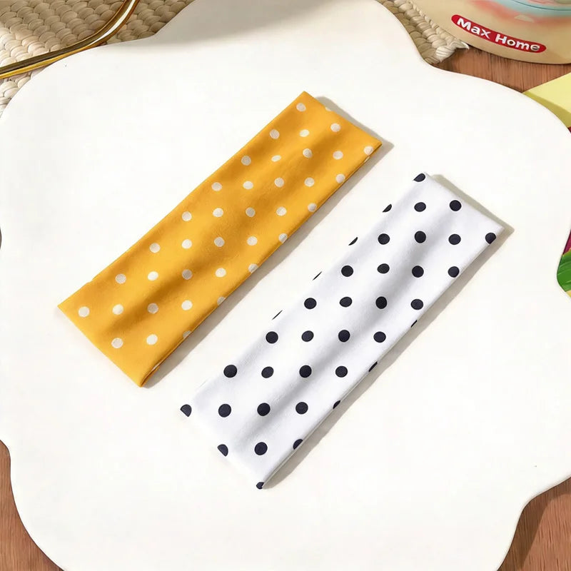 Zwei Stoff-Haarbänder auf weißem Untergrund, eines gelb mit weißen Polkadotierung und eines weiß mit schwarzen Polkadotierung