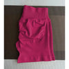 Un short de yoga sans couture, de couleur magenta et taille haute, est posé à plat sur une surface marron texturée.
