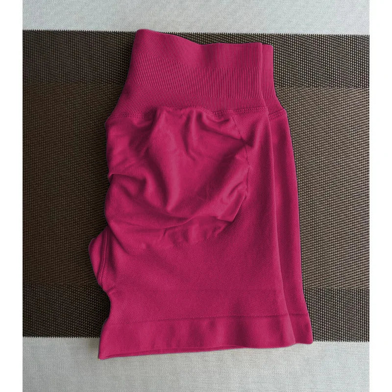 Un short de yoga sans couture, de couleur magenta et taille haute, est posé à plat sur une surface marron texturée.