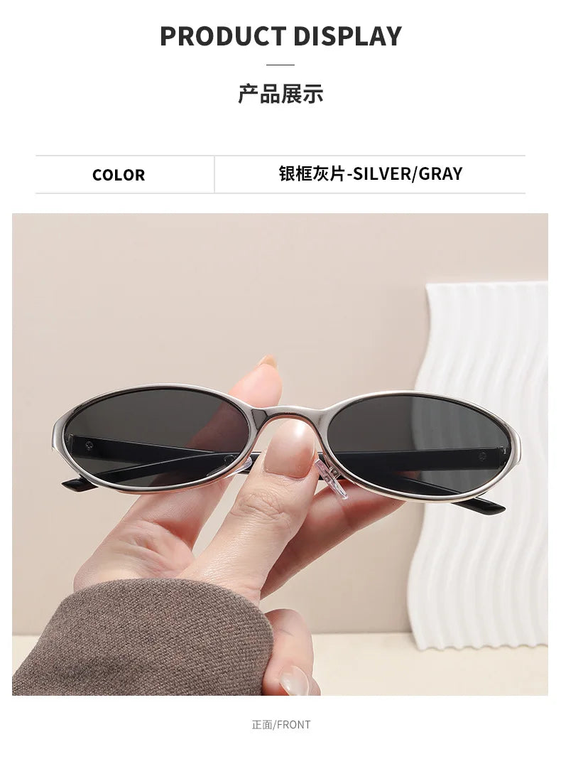 A hand holds a pair of silver/gray retro oval sunglasses against a white background.