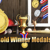 A display of gold, silver, and bronze winner medals with ribbons and a golden trophy on a wooden surface.
