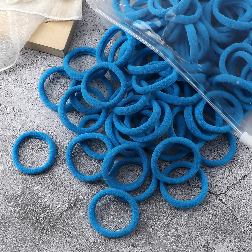 A pile of blue elastic hair bands and a clear plastic tube are shown on a gray surface.