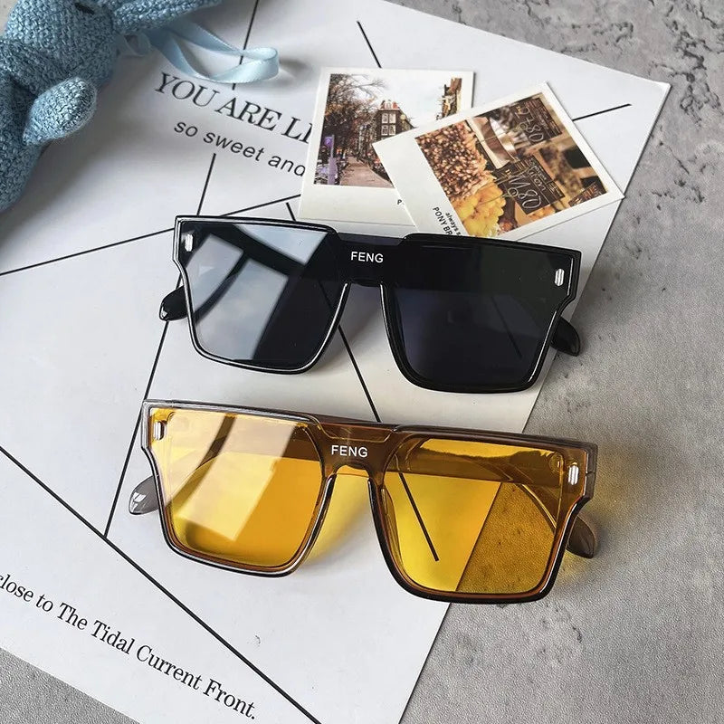 A pair of amber-tinted oversized square sunglasses resting on a white paper with nature photos.