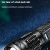 A close-up view of a black tactical LED flashlight with a textured grip and illuminated lens, showing water droplets on the s