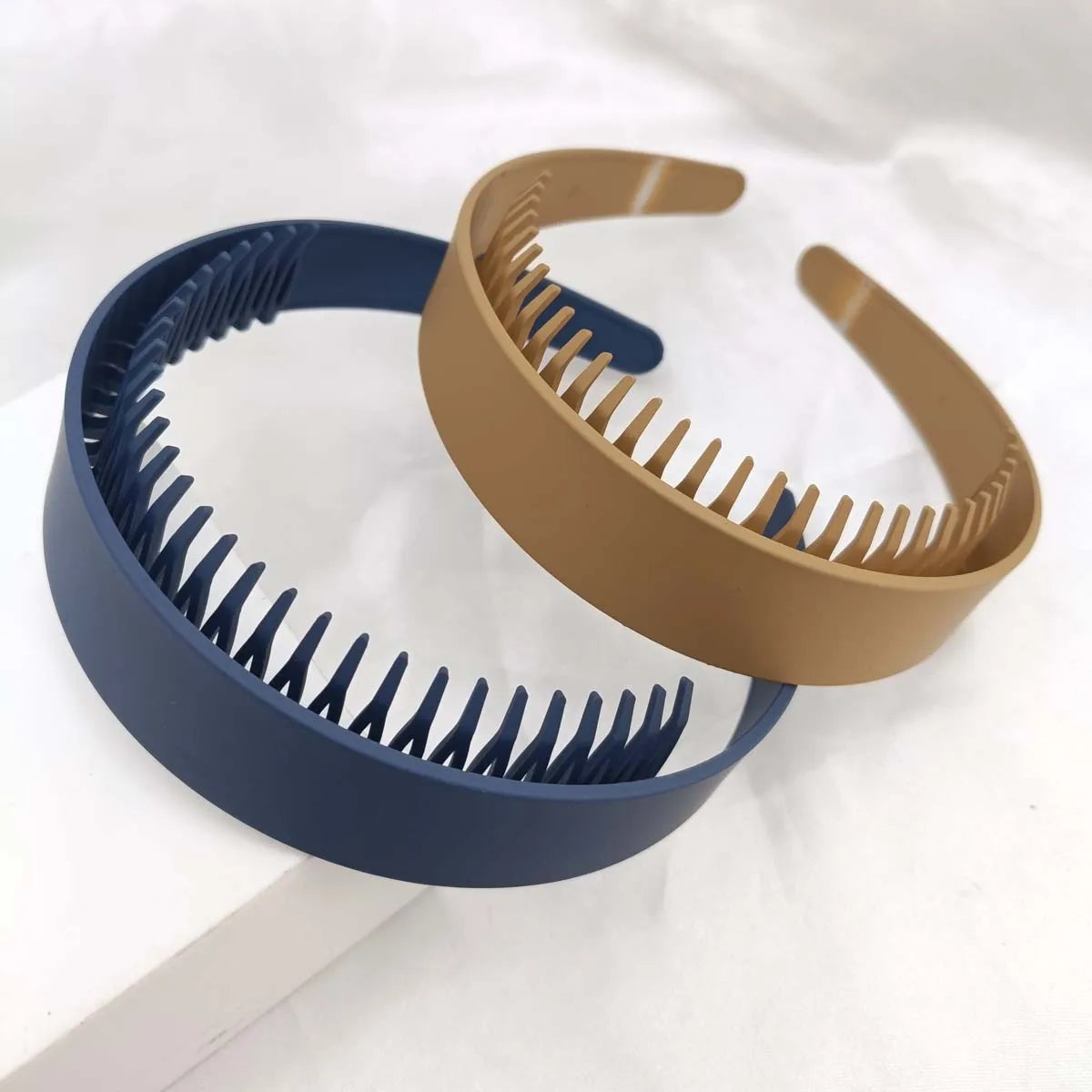Zwei Plastik-Haargummis, eines dunkelblau und eines beige, vor weißem Hintergrund.