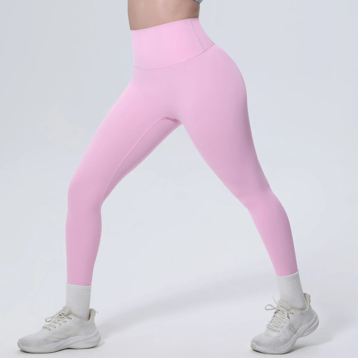A model wearing pink high-waisted quick-drying yoga and fitness leggings with white socks and white sneakers.