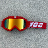 A pair of red goggles with orange-tinted lenses and a white '100' marking, resting on a gray surface.