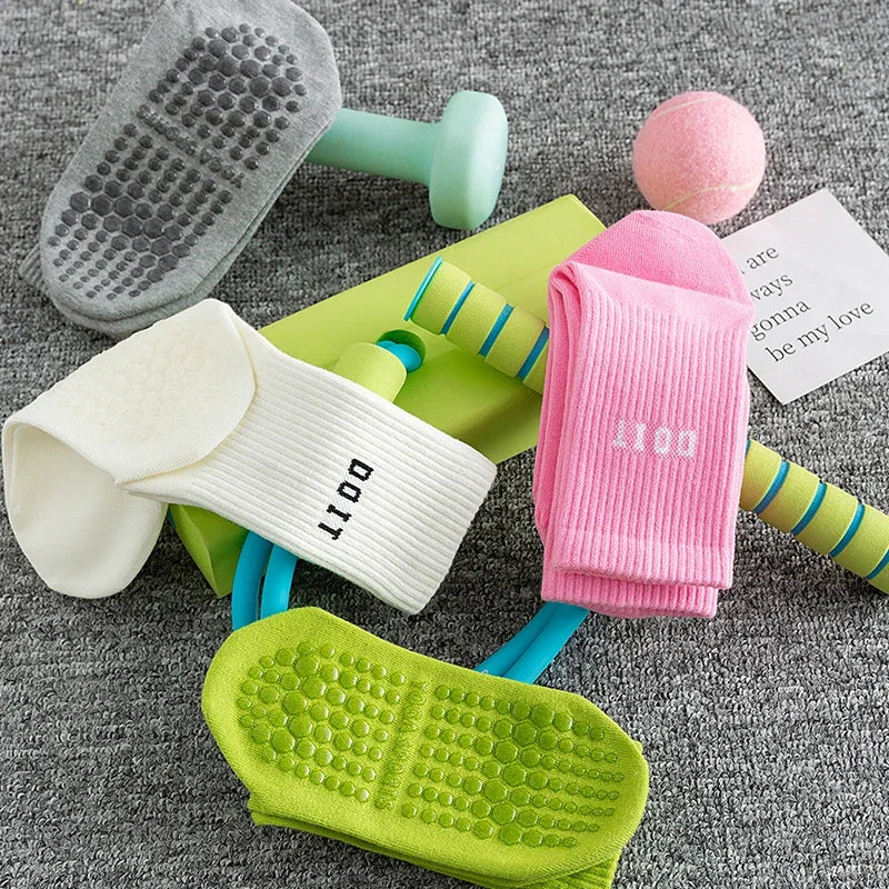 Eine Sammlung farbenfroher Yoga- und Fitnesssocken, darunter eine grau strukturierte Matte sowie rosa, weiße und limettengrün