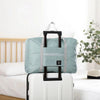 A light blue foldable travel duffel bag with black handles resting on a white suitcase.