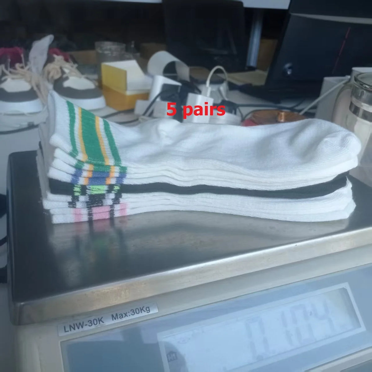 Five pairs of white socks with green, black, and blue stripes are displayed on a metal surface.
