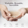 Mains tenant une coque de sein en silicone translucide, dégoulinant de l'eau, montrant la nature lavable et réutilisable du p