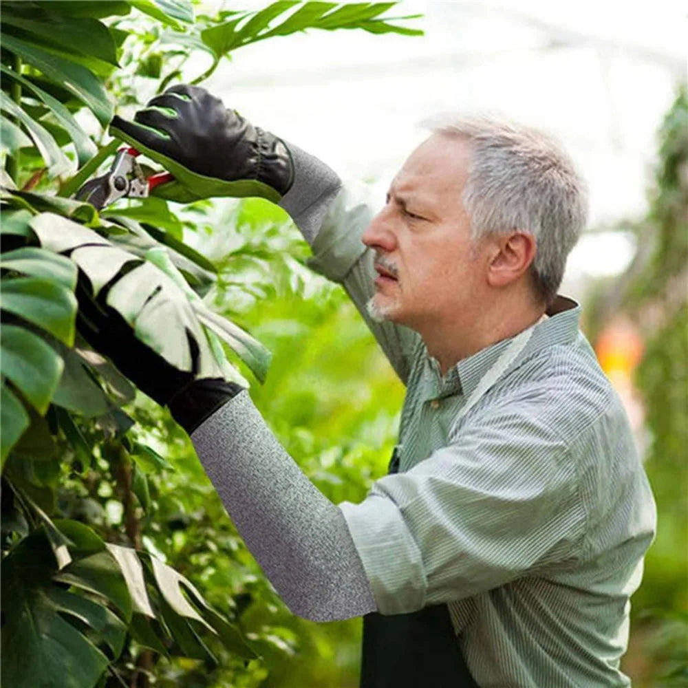 Un hombre con guantes y mangas de protección podando una planta verde en un jardín al aire libre.