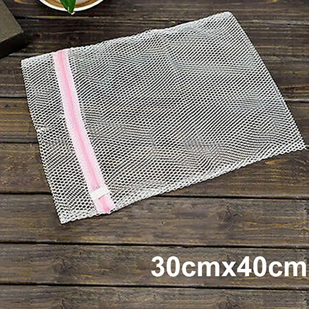 Una bolsa organizadora de ropa de malla rectangular con ribete rosa, exhibida sobre una superficie de madera oscura.