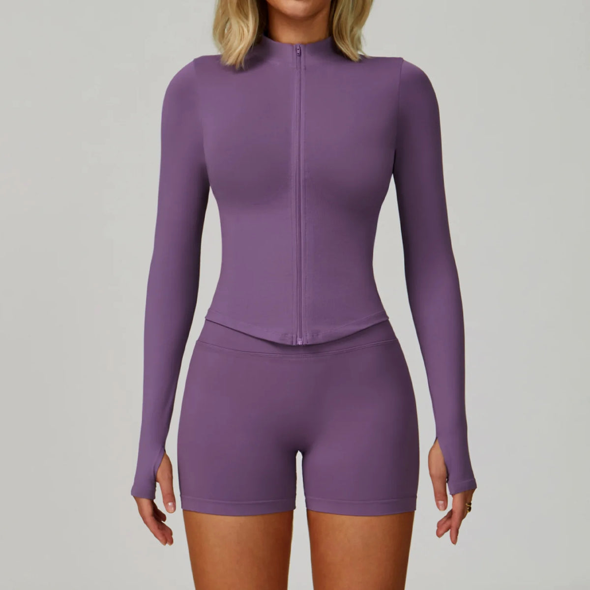 Eine Frau trägt ein durchgehendes lila Langarm-Top und passende Shorts für ein Sport-Yoga-Set.