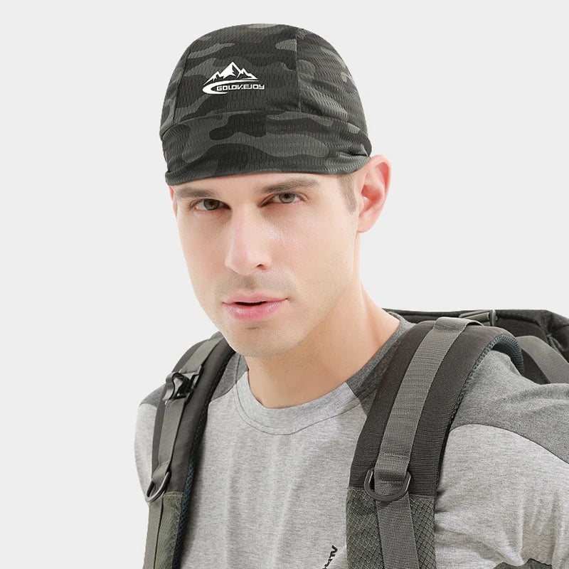 Un hombre vistiendo una gorra de camuflaje con logo de montaña, camiseta gris y mochila.