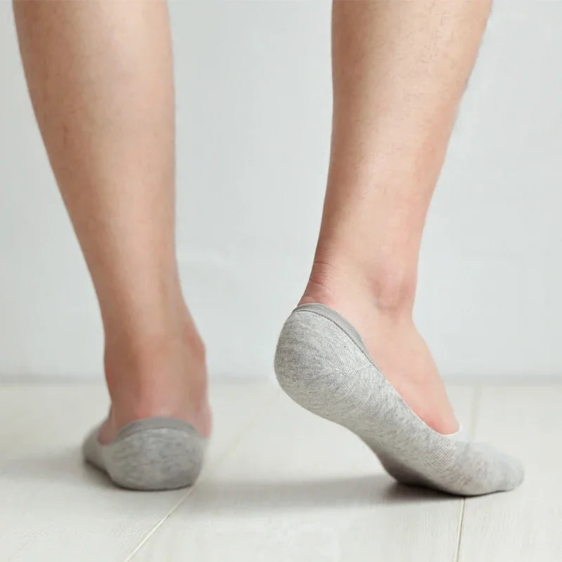Une paire de chaussettes invisibles en silicone gris respirantes, portées pieds nus.