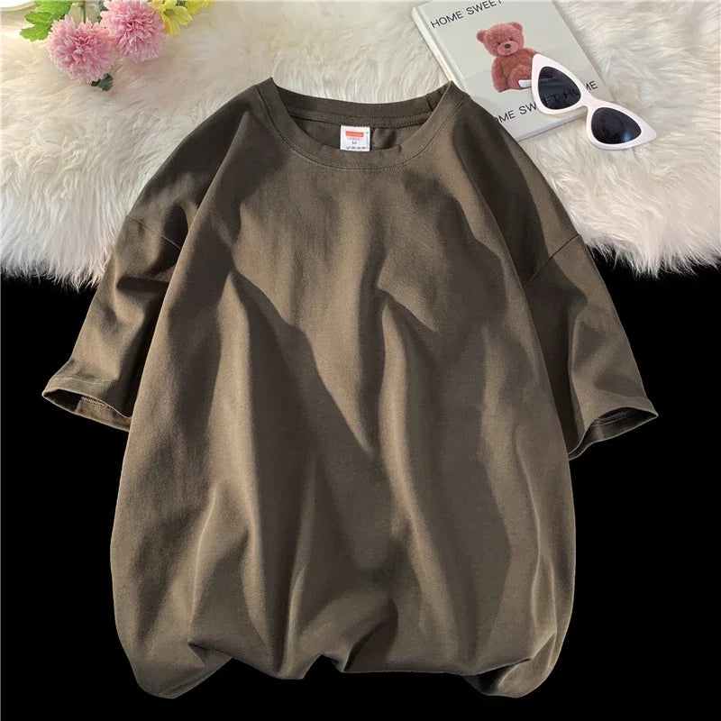 Lockeres olivgrünes, oversized Baumwoll-T-Shirt einer Frau auf einer weißen flauschigen Oberfläche mit Sonnenbrille daneben.