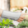 A hand is holding a white pump bottle and a gray ergonomic wrist support brace for joint pain relief.
