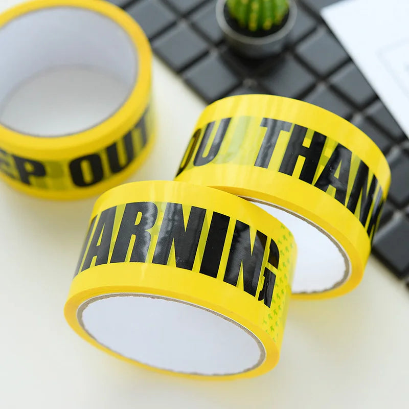 A roll of yellow industrial safety warning tape placed next to a black keyboard and a small cactus.