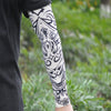 Close-up of a person wearing black clothing and white ice silk tattoo sleeves with black ornamental designs.