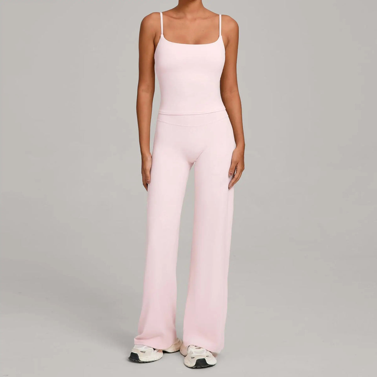 A woman wearing a light pink high-waist yoga and fitness tracksuit set consisting of a tank top and matching trousers.