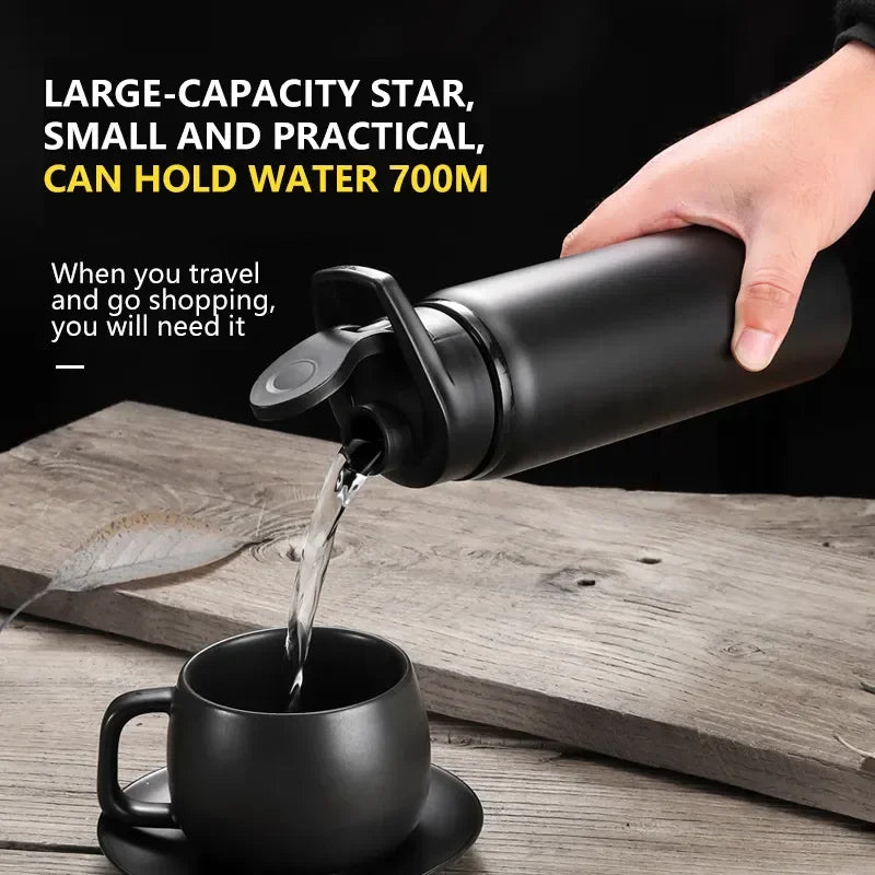 A hand pours water from a black bottle into a mug on a wooden surface.