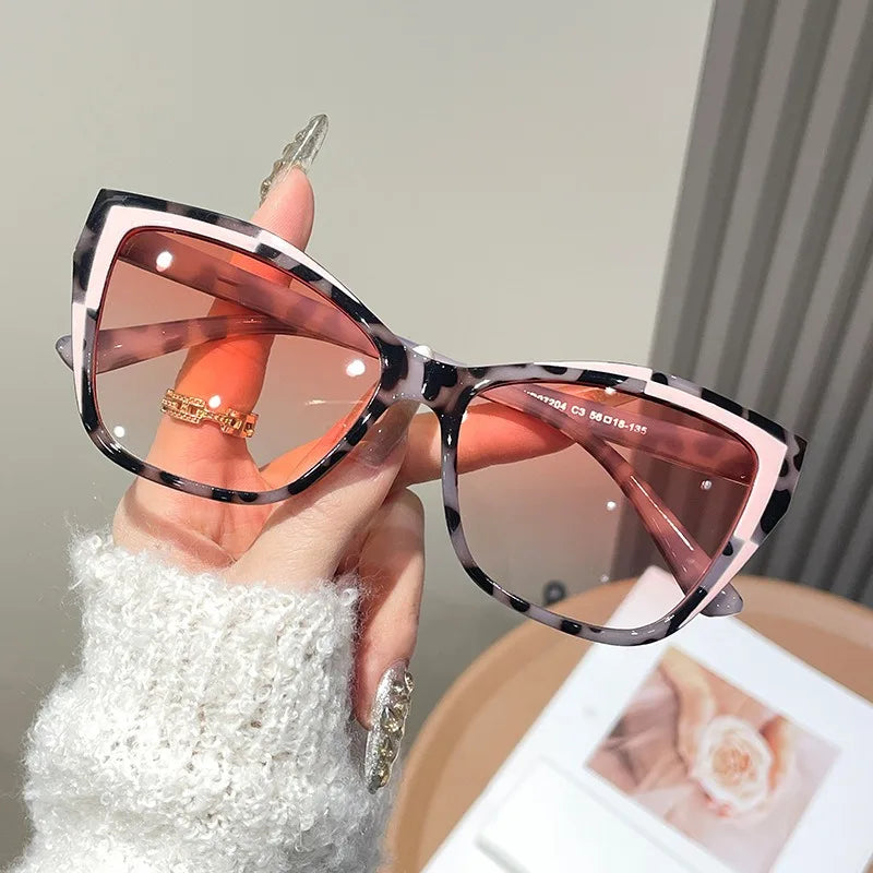 A hand holds a pair of pink and black vintage square cat eye sunglasses against a light background.