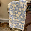 A soft coral fleece face towel with a light blue and cream cloud pattern displayed on a wooden surface.