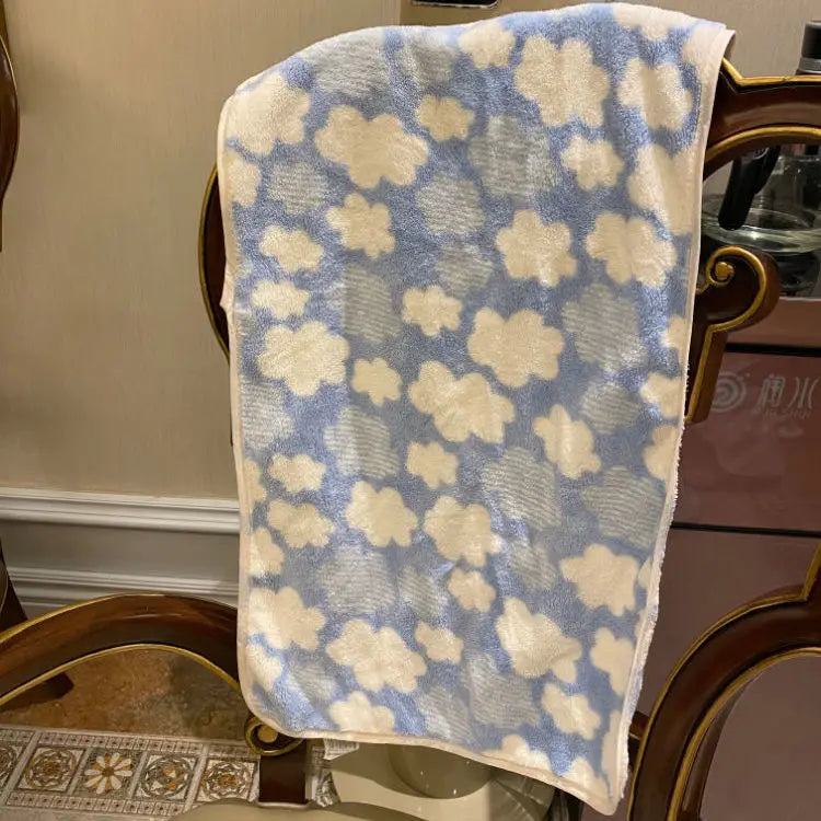 A soft coral fleece face towel with a light blue and cream cloud pattern displayed on a wooden surface.