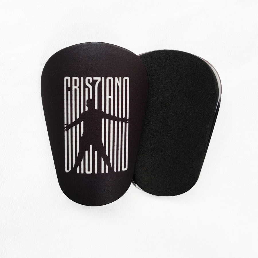 Protectores de espinilla negros mini de fútbol con texto blanco y silueta de una persona.