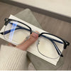 A pair of black-framed, retro square blue light blocking eyeglasses resting on a white card next to a beige sweater.