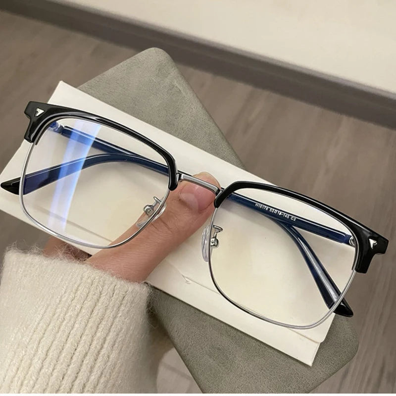 A pair of black-framed, retro square blue light blocking eyeglasses resting on a white card next to a beige sweater.