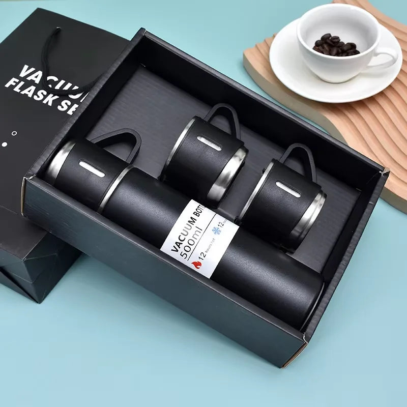 A black vacuum flask in its box with a lid and a cup of coffee on a wooden surface.