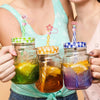 Hand holding three glass jars with silicone straw covers filled with colorful drinks
