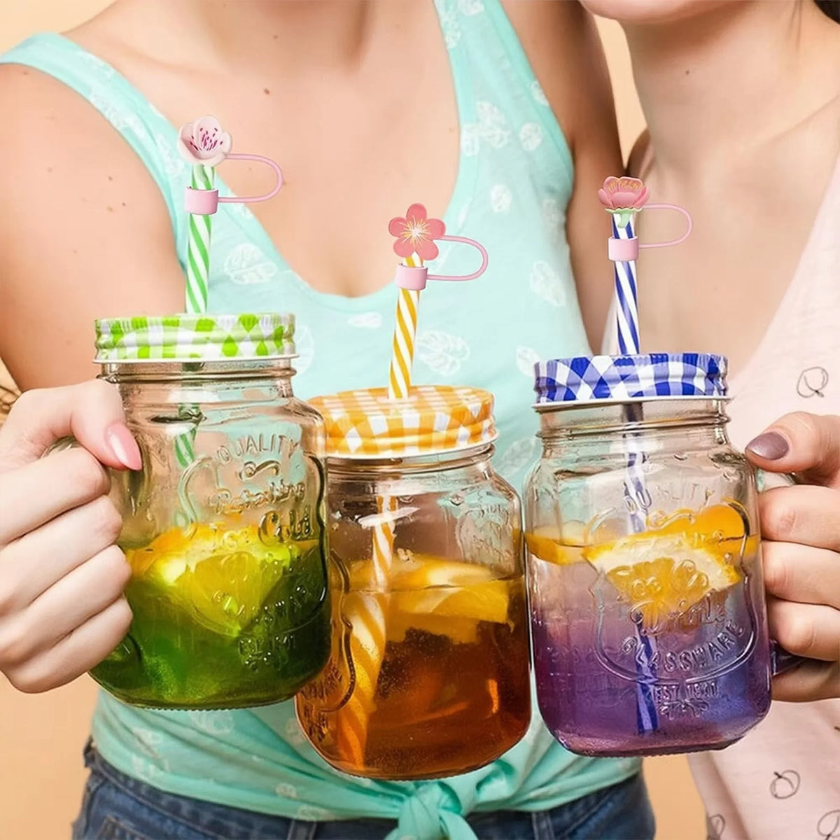 Hand holding three glass jars with silicone straw covers filled with colorful drinks